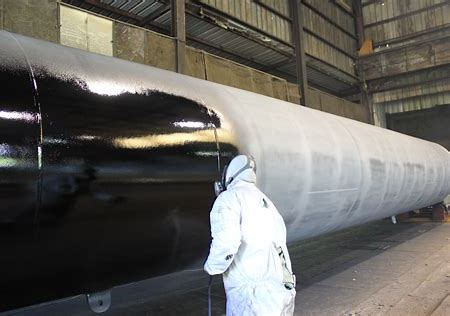 An operator applies a corrosion inhibitor to a large steel pipe.
