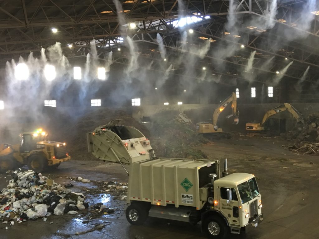 Garbage trucks dumping trash inside an enclosed transfer station.
