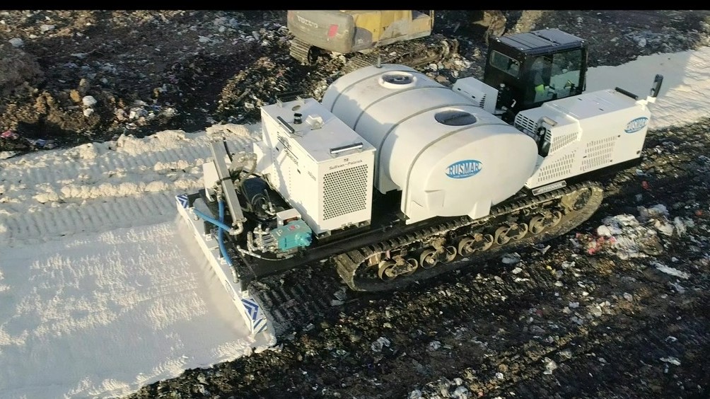 A tracked machine applying aqueous foam cover over a landfill working face.